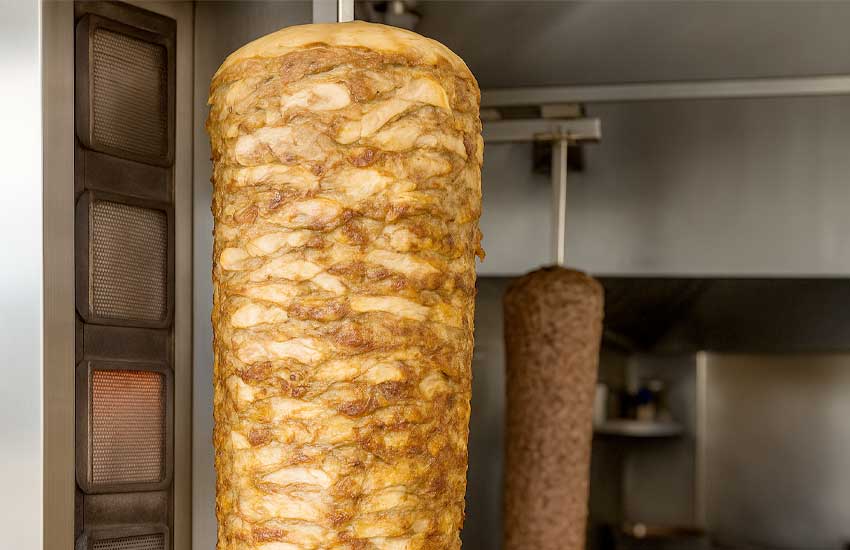 Mięso z kurczaka na rożnie opiekane w elektrycznym opiekaczu do kebaba w lokalu gastronomicznym